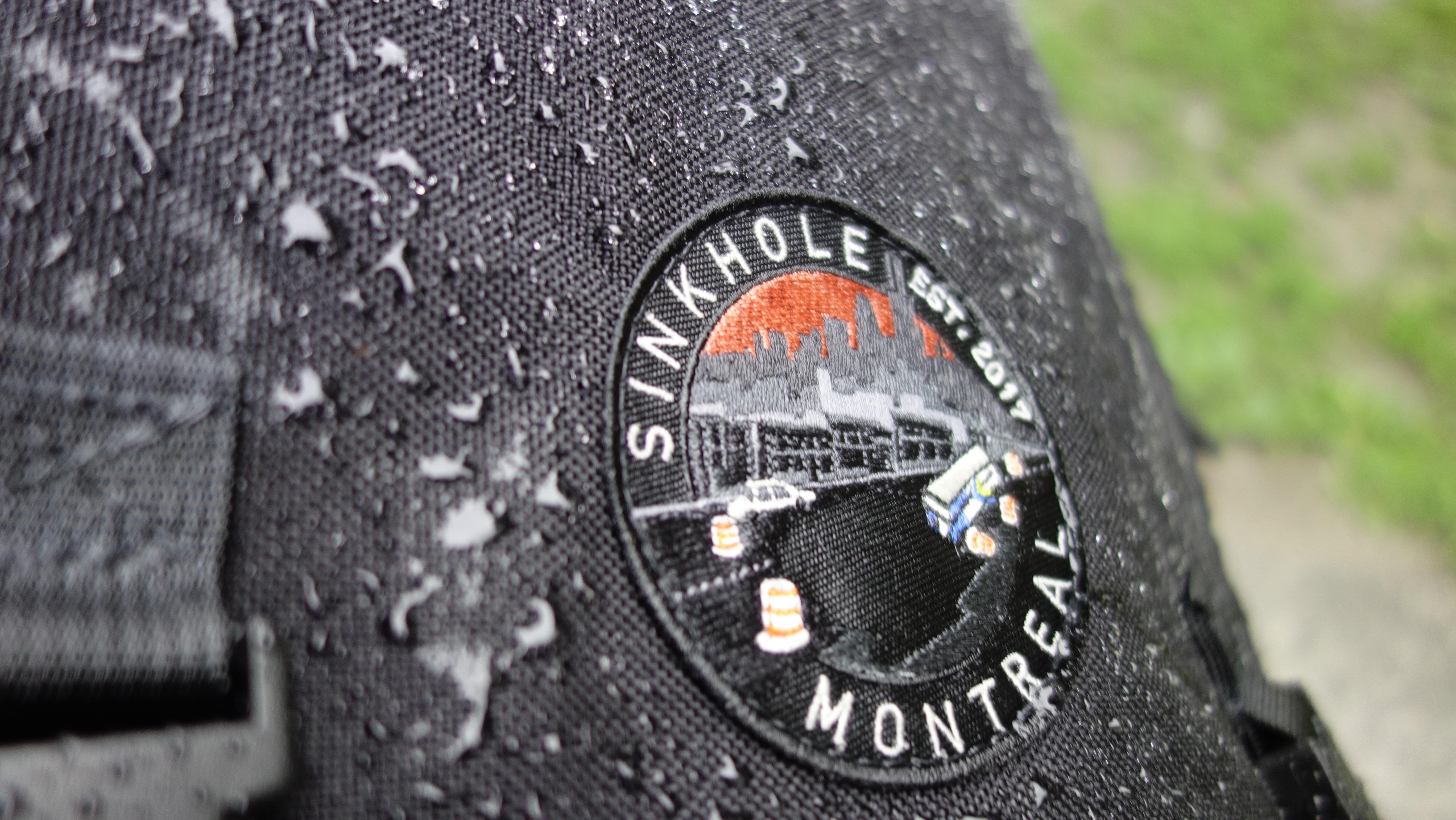 close up the sinkhole logo patch surrounded by beaded rain on black Cordura
